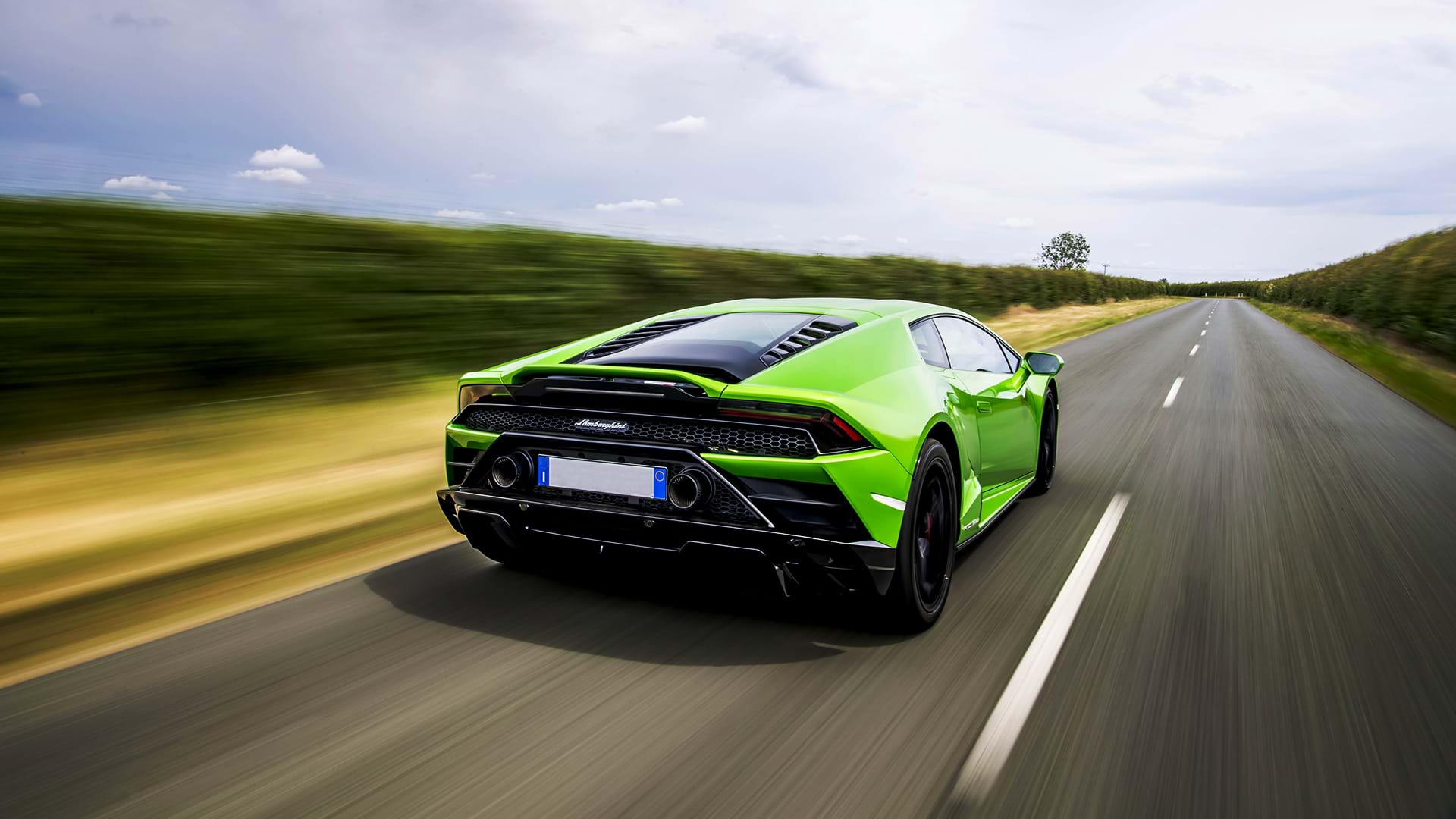 Bright green Lamborghini Huracán Evo speeding down a country road on a sunny day.